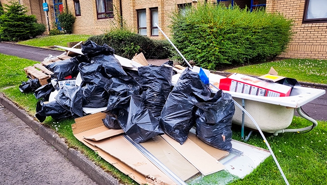 A pile of black trash bags and junk on a lawn in front of an apartment building.