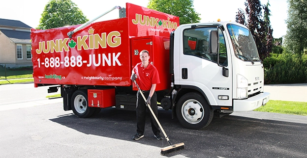 Image of a red Junk King dump truck with an employee using a push broom beside it.